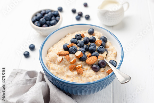 Healthy breakfast oatmeal porridge in bowl with blueberries and almonds on white wooden table background