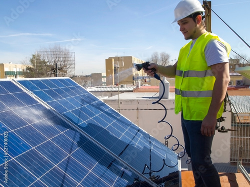 Caucasian attractive young technician cleaning solar panels with a hose photo