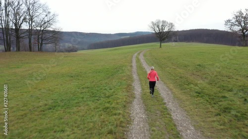 4K aerial video drone point of view, following and flying over sporty woman jogging alone over meadow in rural landscape on overcast day photo