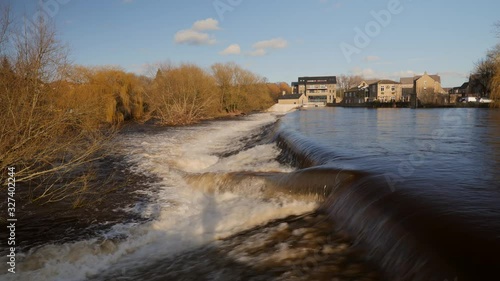 An overflowing river in Yorkshire during the UK floods with a a fast waterfall crashing down stream