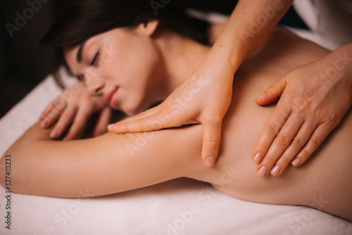 Close-up of young relaxed woman lying down on massage table with close eyes who is given back and shoulder massage at spa salon. Concept of luxury professional massage. Concept of body care.