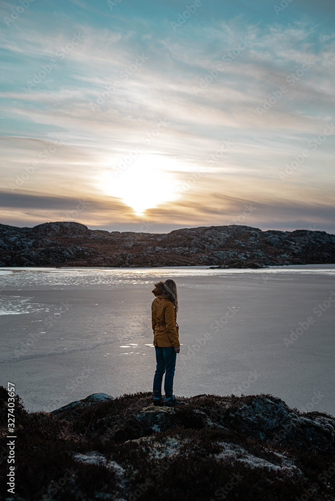 Woman looking at a frozen lake on a beautiful sunny evening in winter Norway.