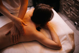Close-up female massage therapist does back massage to young woman in massage room with soft lighting. Concept of luxury professional massage. Concept of body care.