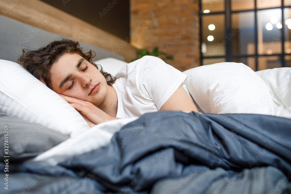 Peacefulness concept. Handsome young man sleeping in bed at modern room Peacefulness concept. Handsome young man sleeping in bed at modern room