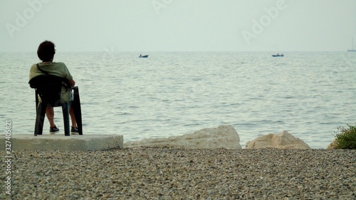 Uomo solo seduto sulla sedia di plastica  in riva al mare photo