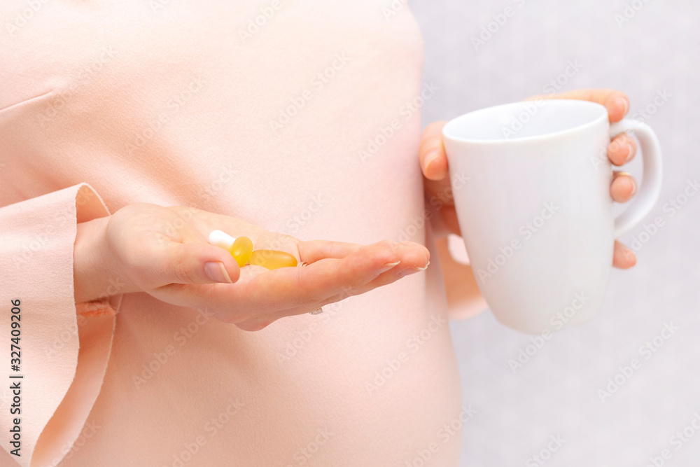 Close-up of pregnant woman holding a pill, vitamins. The concept of pregnancy, healthcare, gynecology, medicine and a healthy lifestyle. Mother is expecting a baby. Nutritional supplements. Close-up of pregnant woman holding a pill, vitamins. The concept of pregnancy, healthcare, gynecology, medicine and a healthy lifestyle. Mother is expecting a baby. Nutritional supplements.