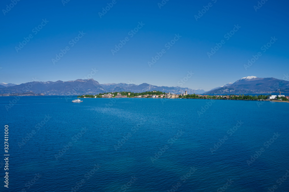 Sirmione island Lake Garda, Italy. The ship heads towards the island. Aerial view. Mountains and blue sky in the background.
