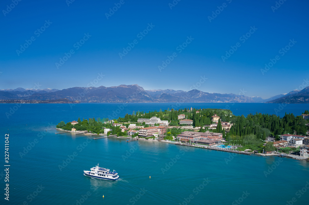 Sirmione island Lake Garda, Italy. The ship is heading from the island. Aerial view. Mountains and blue sky in the background.