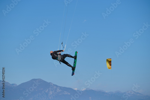 Kitesurfer in wetsuit in  the jump on a background of high mountains in company with Kitesurfers