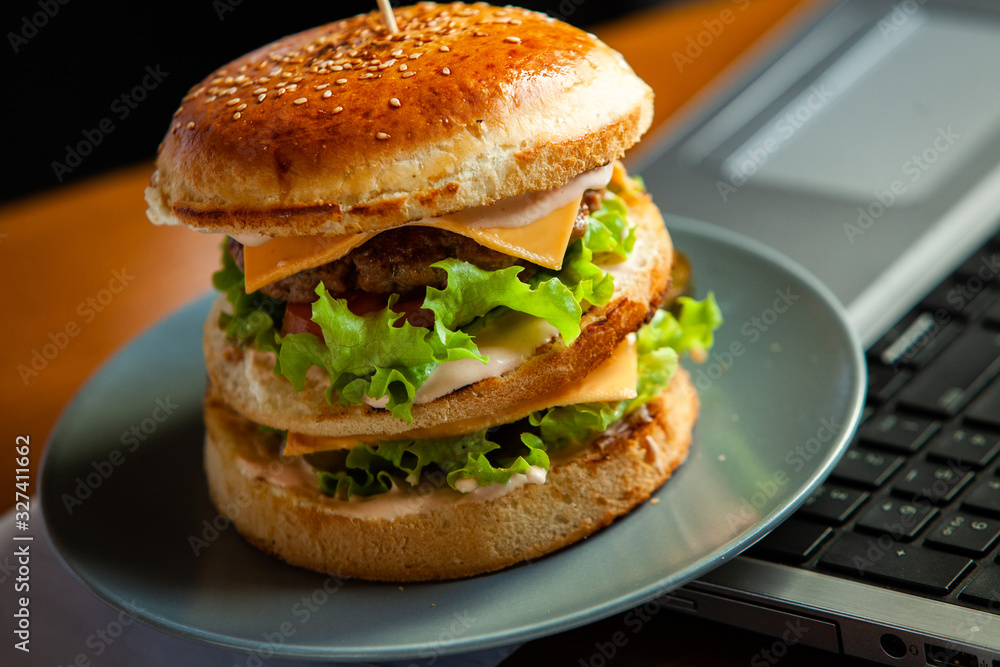 Eating at work place - fast food. burger near laptop. lunch break while you work or sharing online Eating at work place - fast food. burger near laptop. lunch break while you work or sharing online