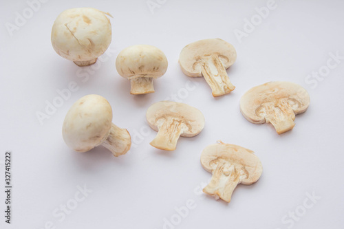 Four raw champignon mushrooms (three whole ones and one cut) at white background