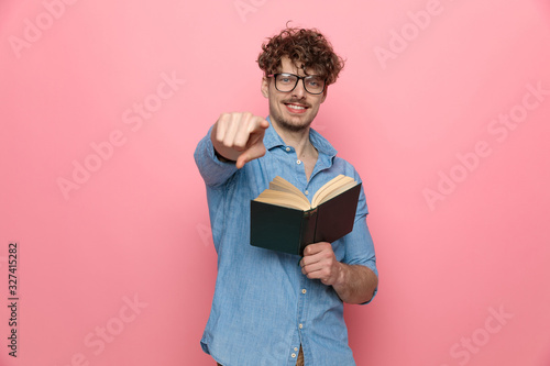 young casual guy in denim shirt holding book and pointing finger