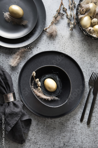 Easter table setting with black and golden decor on grey. Top view.