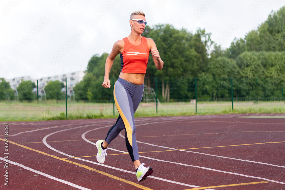 An adult woman runs at the stadium, in sports clothes. An adult woman runs at the stadium, in sports clothes.