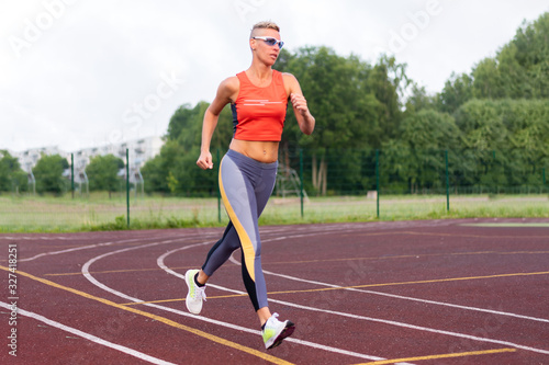 An adult woman runs at the stadium, in sports clothes. © Artsiom P