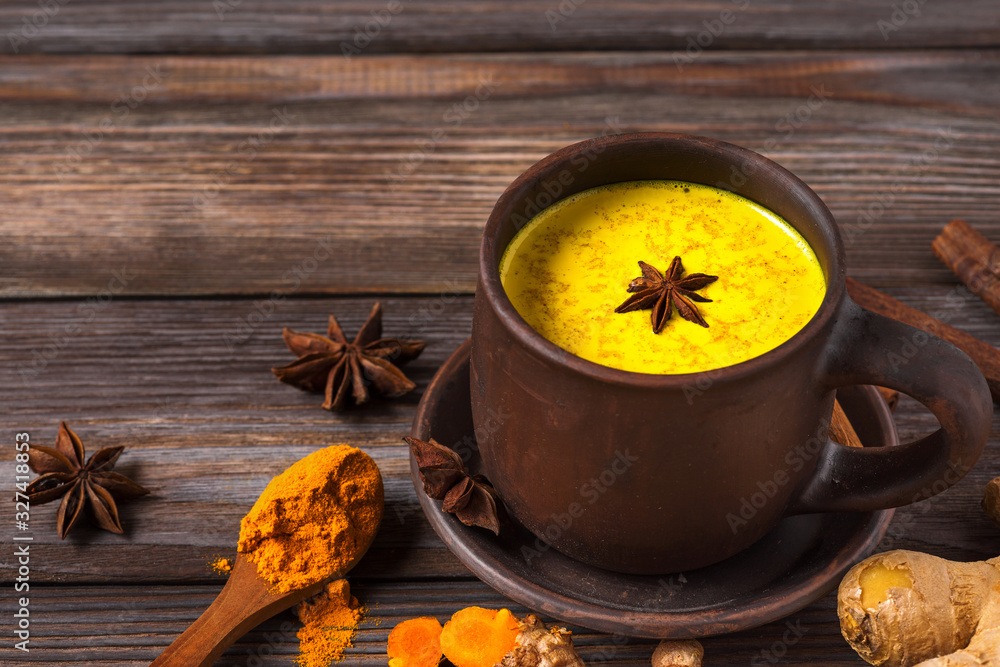 Golden milk or turmeric latte made with curcuma, star anise, ginger and cinnamon on rustic wooden table. Healthy drink Golden milk or turmeric latte made with curcuma, star anise, ginger and cinnamon on rustic wooden table. Healthy drink