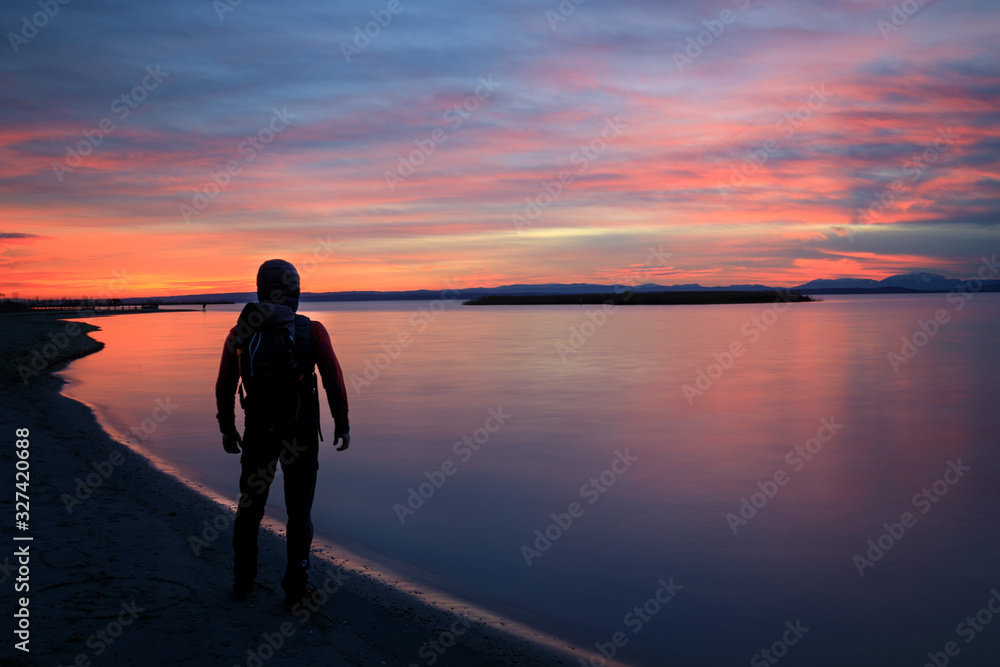 hiker with bagpack standing at lake during sunset