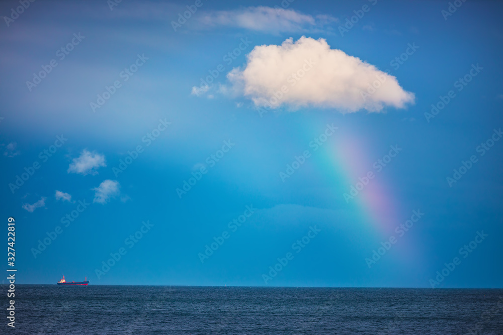 Rainbow in the sea and sailing cargo ship