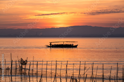 Sunset pier Albufera Valencia tourist ride boat reflections orange sky in the lake Naural Park Spain. traditional fishing nets in the water
