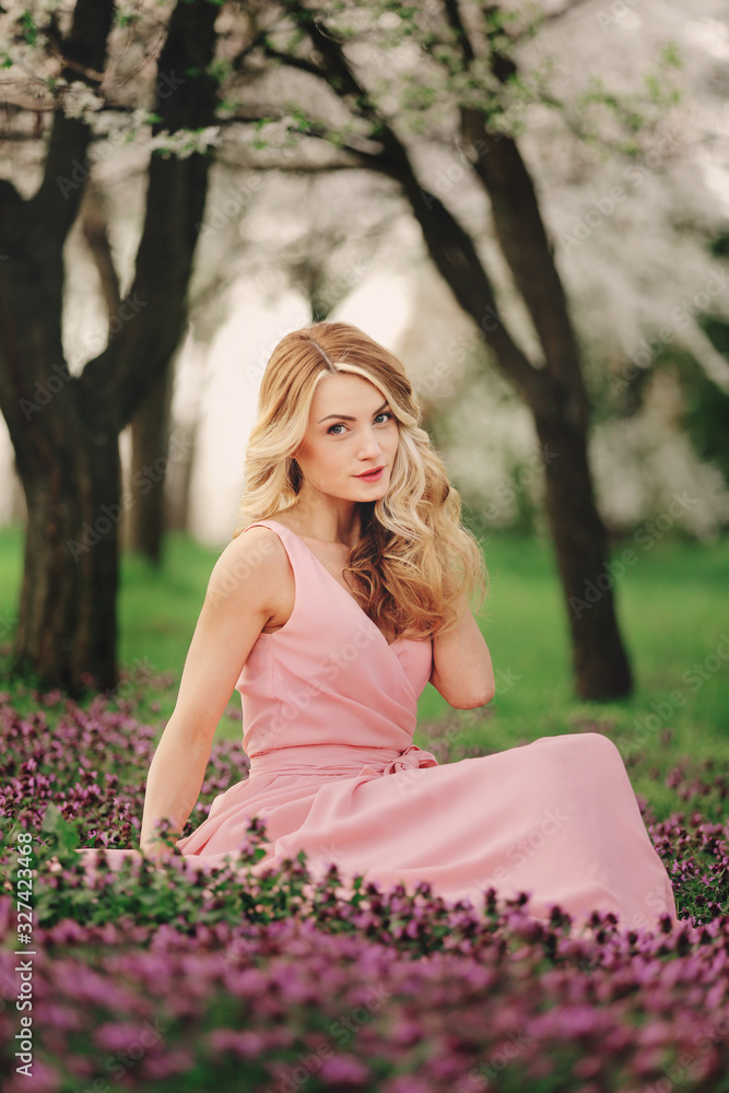 Beautiful blonde young woman in colorful flowers. girl with make-up and hairstyle in pink dress in blossoming spring park. Art work of romantic woman .Pretty tenderness model looking at the camera Beautiful blonde young woman in colorful flowers. girl with make-up and hairstyle in pink dress in blossoming spring park. Art work of romantic woman .Pretty tenderness model looking at the camera