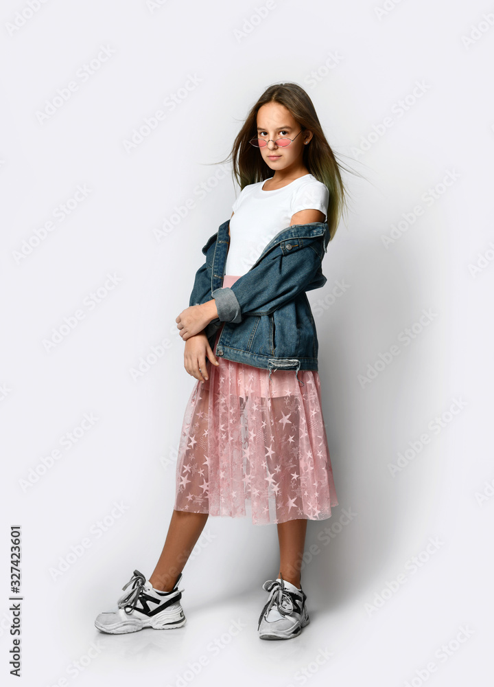 Fototapeta premium Young smiling teen girl in stylish casual clothes, sneakers and pink sunglasses standing and looking at camera