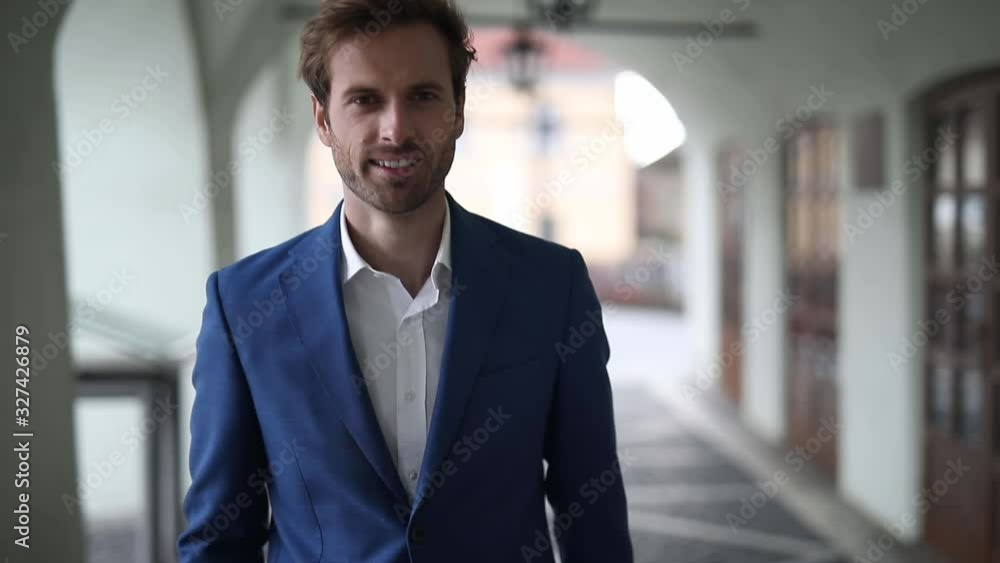 handsome businessman wearing navy suit walking with style while looking at camera happy outside in the city handsome businessman wearing navy suit walking with style while looking at camera happy outside in the city