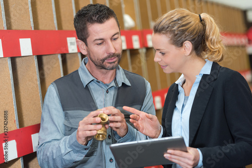 hardware store clerk showing pumbing fittings to woman holding tablet photo