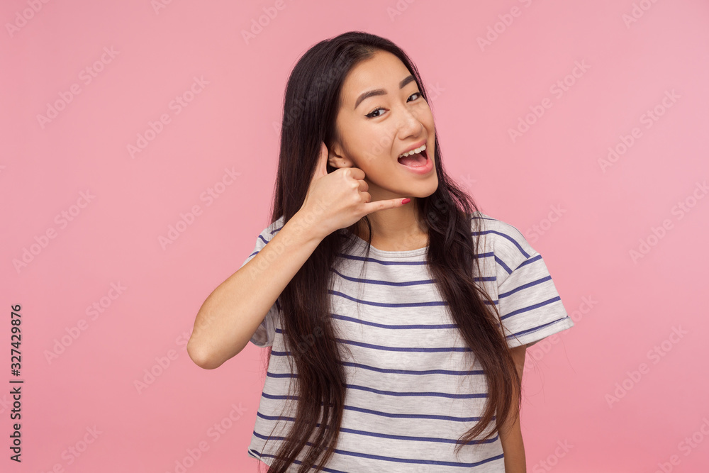 Let's communicate! Portrait of happy cute girl with long brunette hair making call me gesture with hand shaped like telephone, showing dial my number. indoor studio shot isolated on pink background Let's communicate! Portrait of happy cute girl with long brunette hair making call me gesture with hand shaped like telephone, showing dial my number. indoor studio shot isolated on pink background