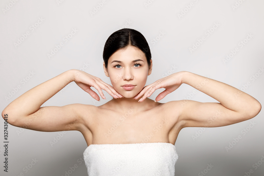 Obraz premium Pretty brunette girl in bath towel touching her tender chin skin isolated light background