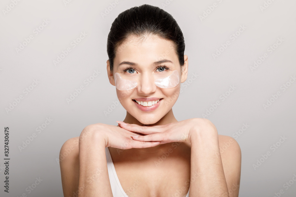 Cute brunette model posing with hands under chin and pore strips on cheekbones isolated light background Cute brunette model posing with hands under chin and pore strips on cheekbones isolated light background