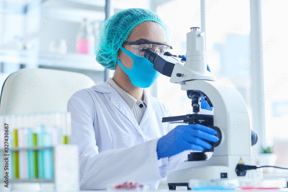 Side view portrait of female scientist looking in microscope while working on research in medical laboratory, copy space Side view portrait of female scientist looking in microscope while working on research in medical laboratory, copy space