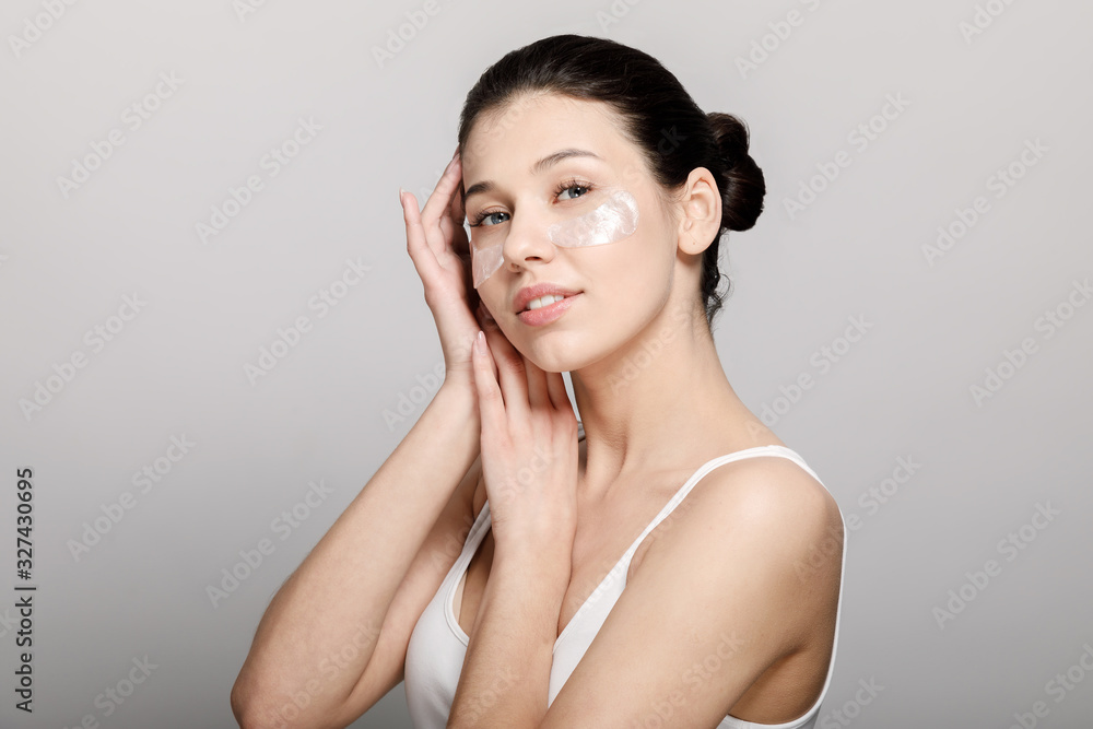Cute brunette young woman in white vest posing dreamingly with pore strips on cheekbones isolated light background Cute brunette young woman in white vest posing dreamingly with pore strips on cheekbones isolated light background