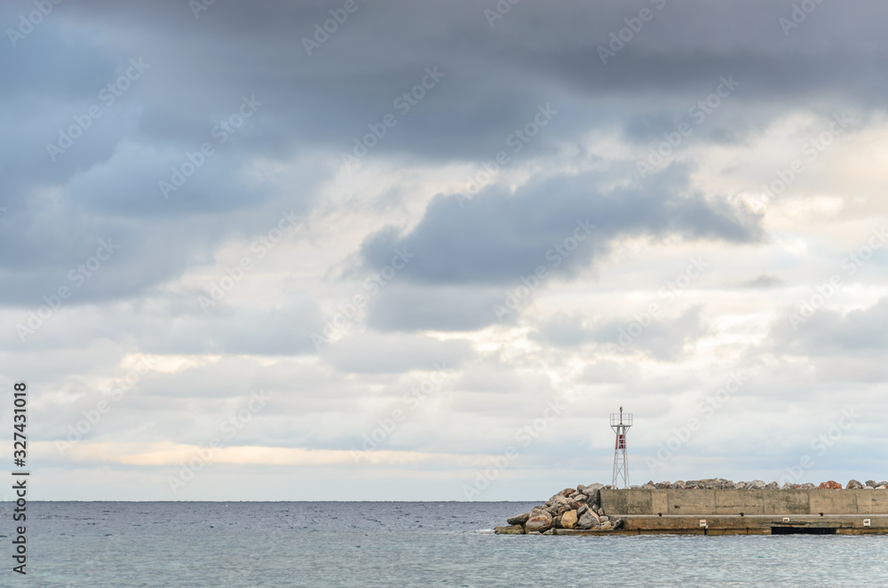 A concrete breakwater with a beacon on a calm overcast day