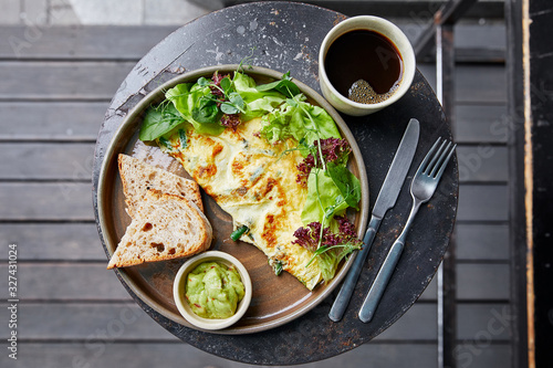 fried eggs with basil, salad and herbs, sauce and white bread, a cup of coffee, amlet, knife and fork, on a table