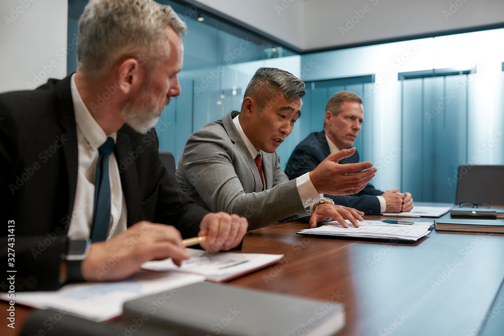 Discussing contract details. Multicultural business team in formal wear working together while sitting at office desk. Discussing project details at meeting Discussing contract details. Multicultural business team in formal wear working together while sitting at office desk. Discussing project details at meeting