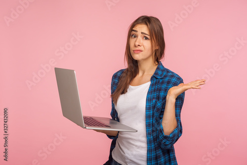 Photography Oops, it doesn't work! Frustrated girl in checkered shirt holding laptop and raising hand in helpless gesture, worried about software bug, program error