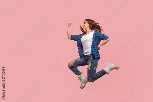 Full length of joyful happy stylish girl in checkered shirt and ripped jeans running in air, hurrying to catch sale, flying and rushing for her dream. indoor studio shot isolated on pink background