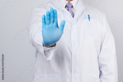 male doctor in a white coat and blue sterile gloves shows a stop gesture