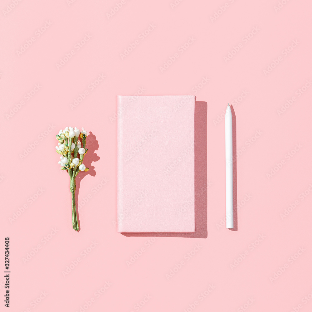 Minimalistic card mockup with empty pink notebook, white pen, blossom flower branch on pink background. Spring feminine blogger concept. Flat lay, square image, top view, copy space.