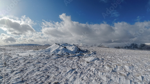 A scenic view of snowy mountain summit trig point cairn under a majestic blue sky and white clouds photo