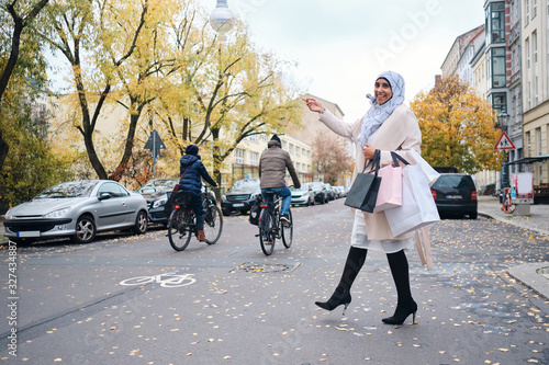 Young smiling Arabic woman in hijab happily walking through street with shopping bags photo