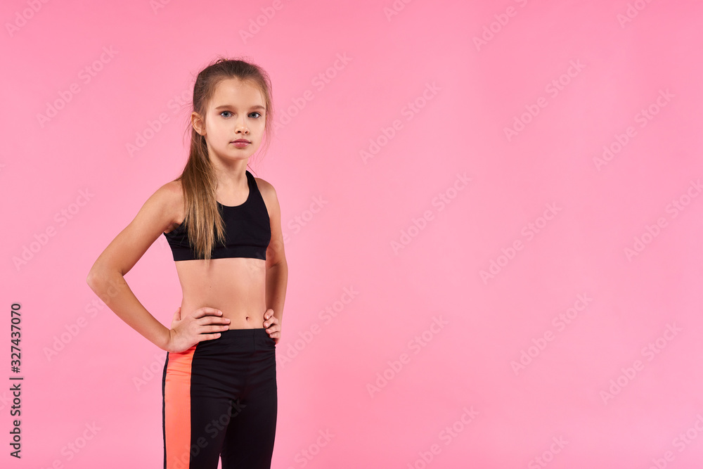 Health and Fun. A cute kid, girl is engaged in sport, she is looking at camera while getting ready to exercise. Isolated on pink background. Fitness, training, active lifestyle concept. Health and Fun. A cute kid, girl is engaged in sport, she is looking at camera while getting ready to exercise. Isolated on pink background. Fitness, training, active lifestyle concept.