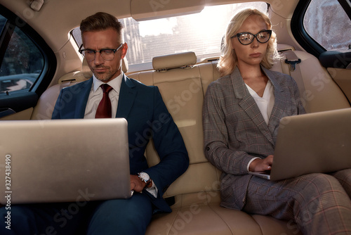 Business professionals. Two colleagues in classic wear working on their laptops while sitting in the car © Svitlana