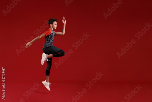 Cardio training. A teenage boy is engaged in sport, he is looking aside while jumping. Isolated on red background. Fitness, training, active lifestyle concept. Horizontal shot