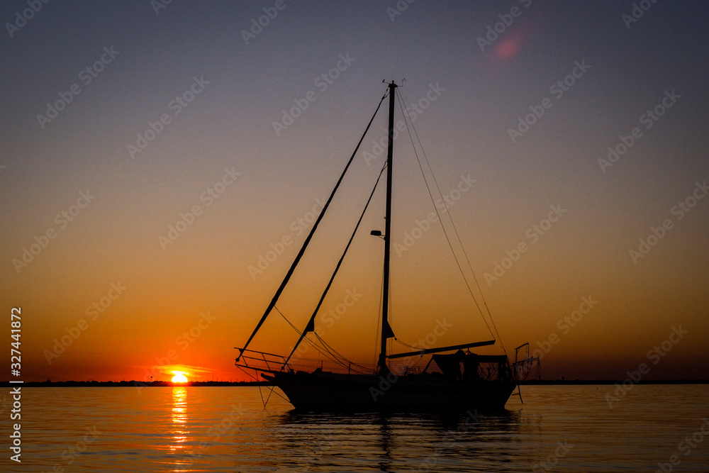 Cutter rigged sailboat with clipper bow and red canvas at sunrise or sunset
