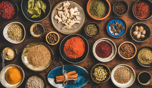 Flat-lay of spices in bowls and plates over rusty background, top view. Black pepper, allspice, cloves, thyme, cumin, sesame, star anise, ginger, cinnamon, cardamom, mahlep, smoked salt, rosemary, bay photo