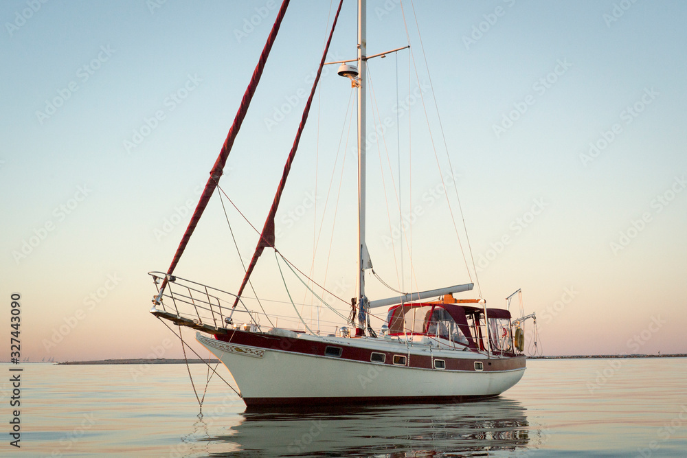 Cutter rigged sailboat with clipper bow and red canvas at sunrise or sunset