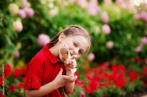 pretty cute girl in a red dress eating ice cream in the park on a summer evening