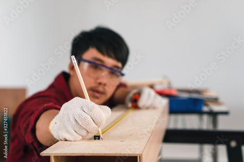 asian male carpenter measuring and marking wood piece for making DIY furniture at home workshop photo