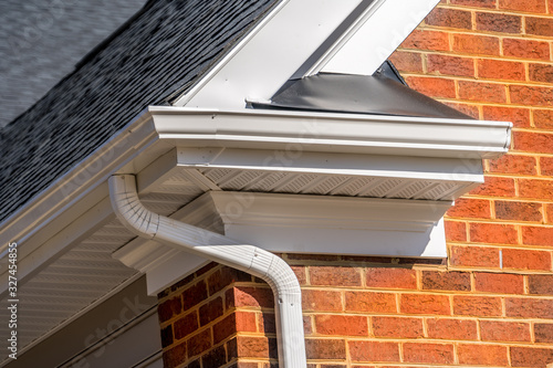 Closeup view of white gutter system with soffit vent, gutter guard, drop outlet, downspout, vinyl elbows, decorative trim molding, on the corner of a brick luxury house in America